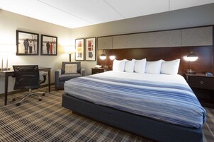 A hotel room with a large bed, a desk, a chair, and two framed pictures on the wall.