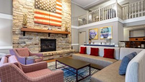 A spacious living room with a stone fireplace, a balcony, and a dining area. - AmericInn by Wyndham Madison South (Madison)