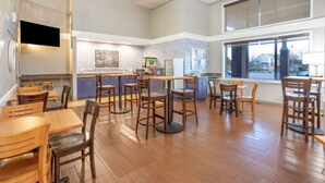 A spacious restaurant with high ceilings, wooden flooring, and a large window offering a view of the outside. - AmericInn by Wyndham Madison South (Madison)