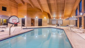 An indoor swimming pool with a basketball hoop, lounge chairs, and a wooden ceiling. - AmericInn by Wyndham Madison South (Madison)