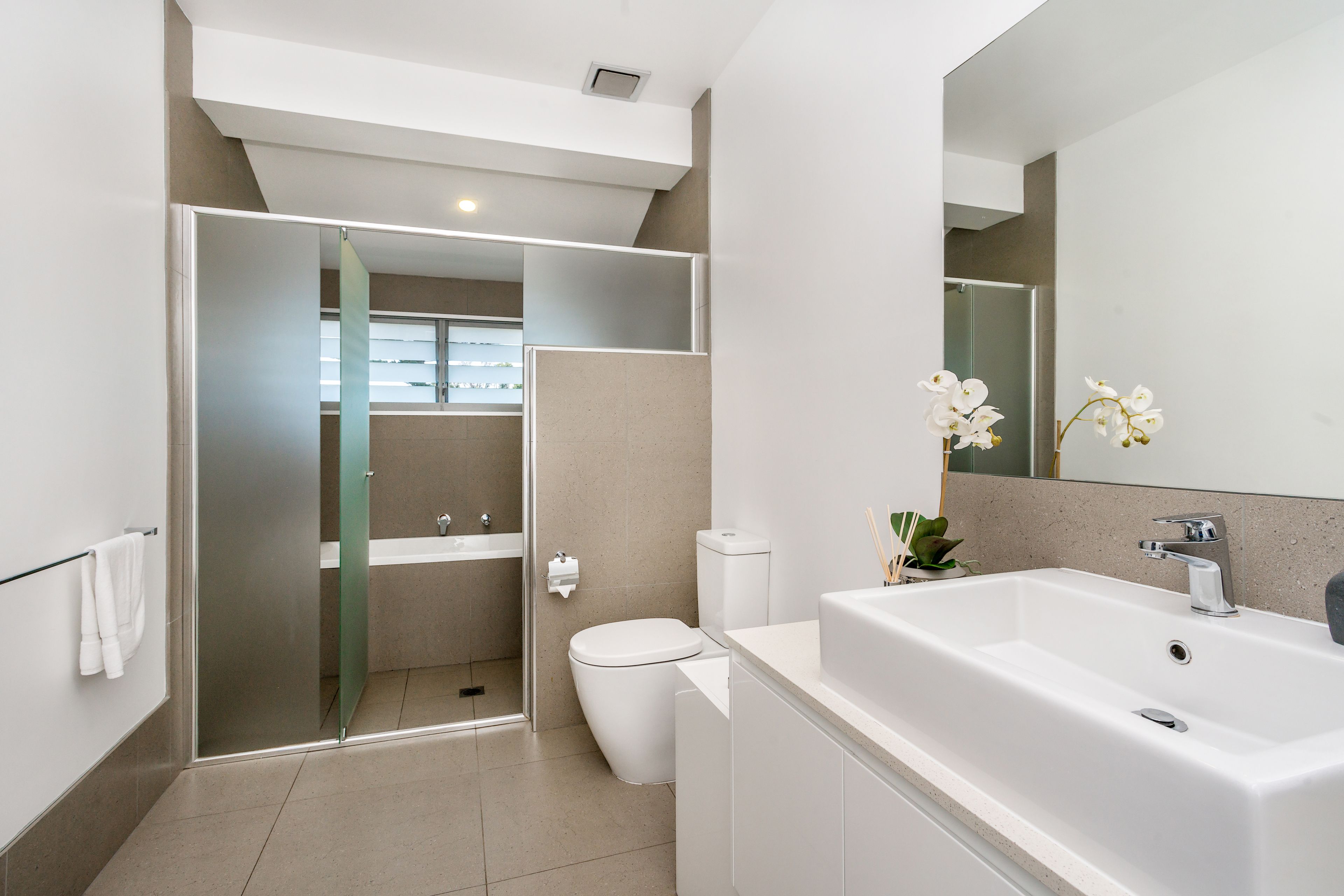 A modern bathroom with a glass shower enclosure, a white toilet, and a large sink with a mirror above it.