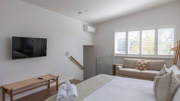 A modern bedroom with a large bed, a bench, a TV, and a window with blinds.