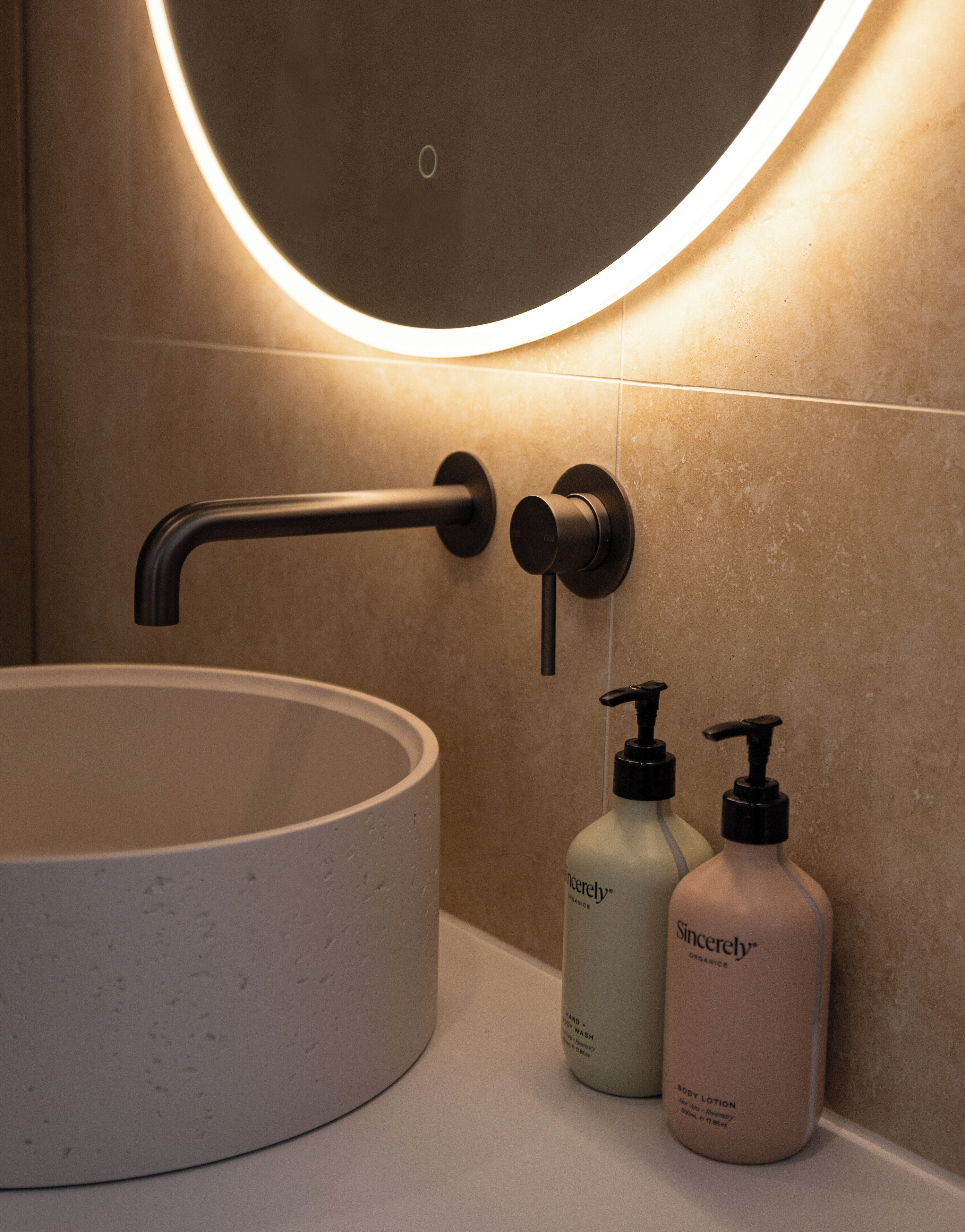 Ein Badezimmer mit einem runden Waschbecken, einem modernen Wasserhahn und zwei Flaschen Körperlotion.