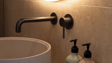 Ein Badezimmer mit einem runden Waschbecken, einem modernen Wasserhahn und zwei Flaschen Körperlotion.