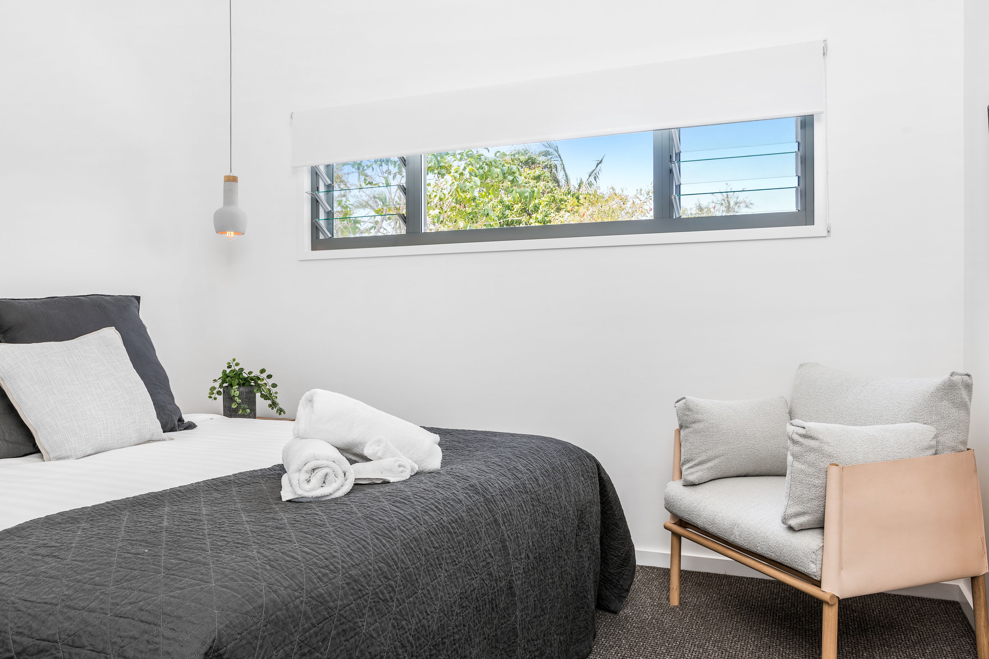 A neatly arranged bedroom with a bed, a chair, a window with a view, and a hanging light fixture.