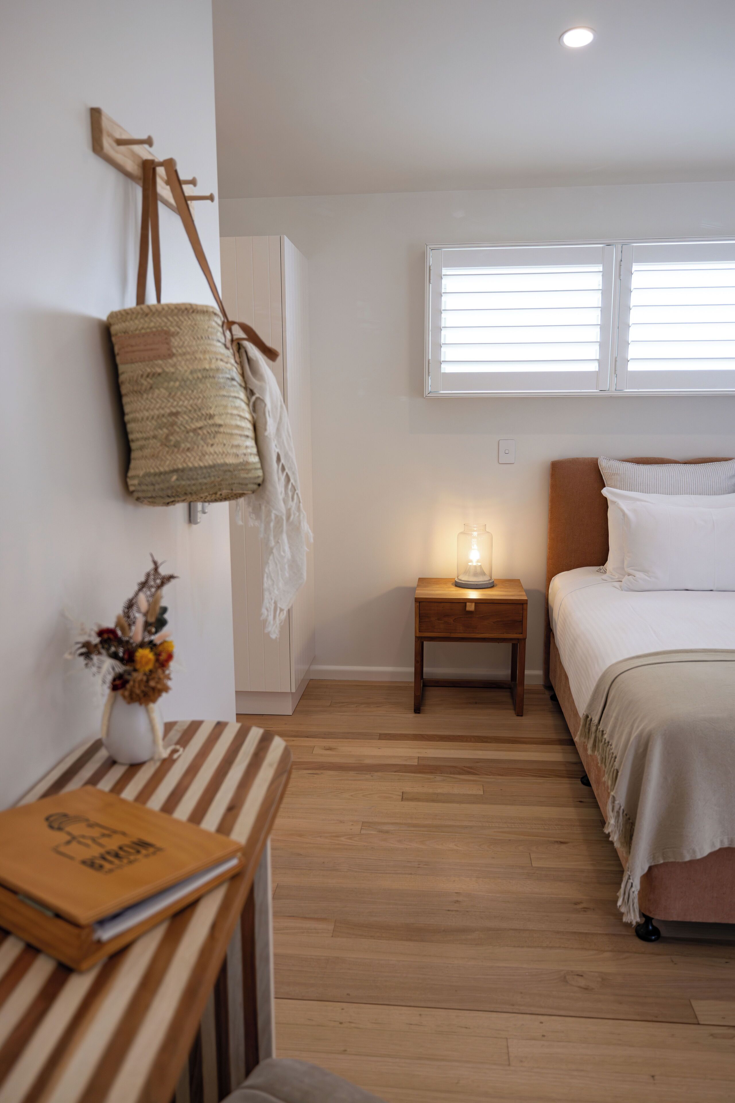 A bedroom with a bed, bedside table, lamp, and a wall-mounted basket.