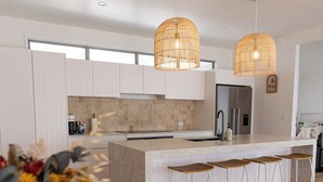 Une cuisine moderne avec des meubles blancs, un îlot central doté de tabourets et deux lampes suspendues.