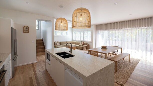 Une cuisine moderne dotée d’un îlot central, un coin repas avec une table et des chaises en bois, et un espace de vie comprenant un canapé et un escalier menant à l’étage.