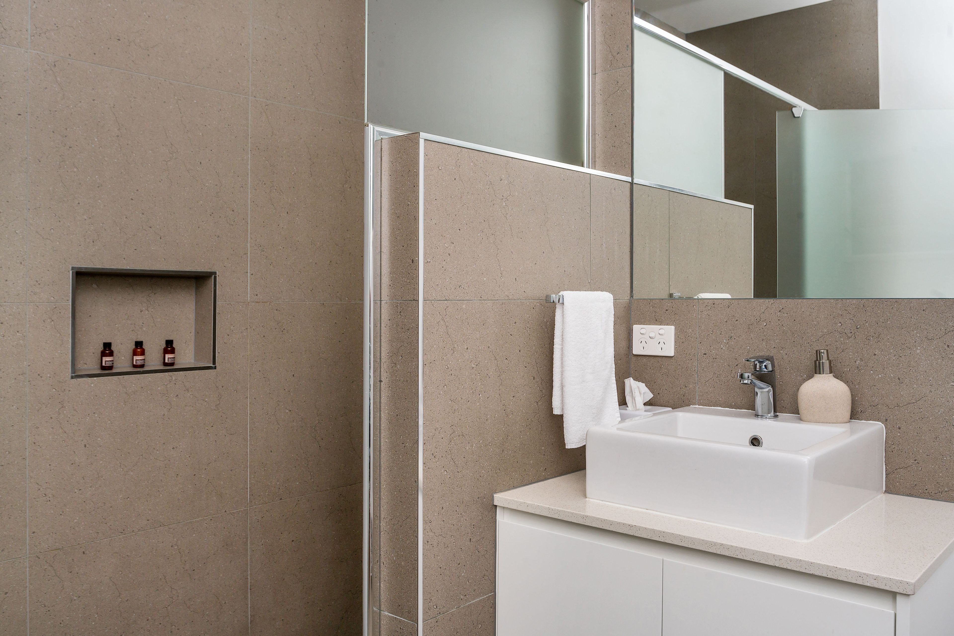 A modern bathroom with a large mirror, a white sink, and a glass shower enclosure.