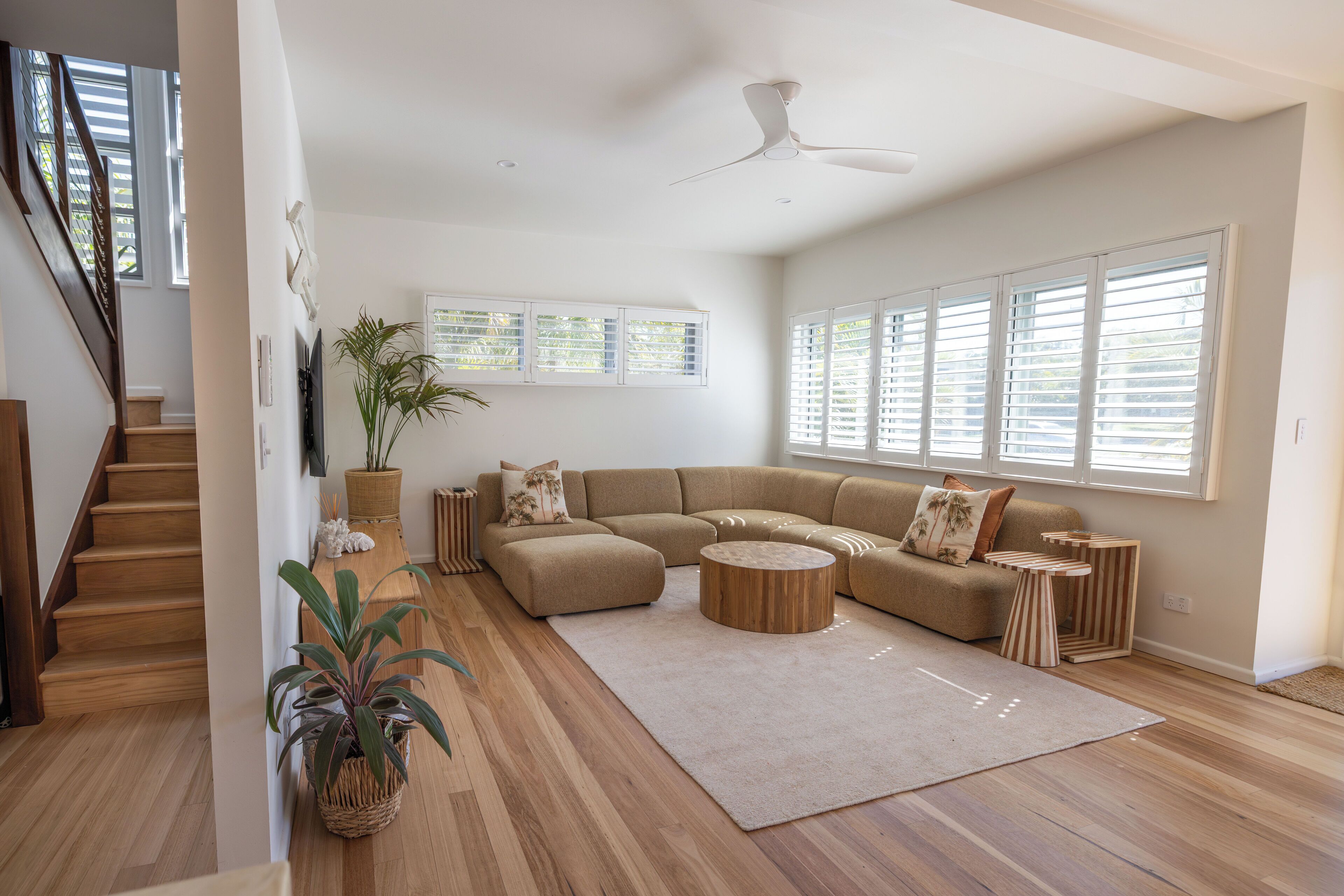 Amplia sala de estar con un sofá modular grande, una mesa de centro de madera y una escalera que conduce a otro nivel.