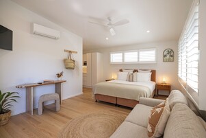 Un dormitorio moderno con cama, mesitas de noche, escritorio, ventilador de techo y ventana con persianas.