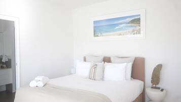 A bedroom with a bed, pillows, a painting of a beach, and a small decorative item on the nightstand.