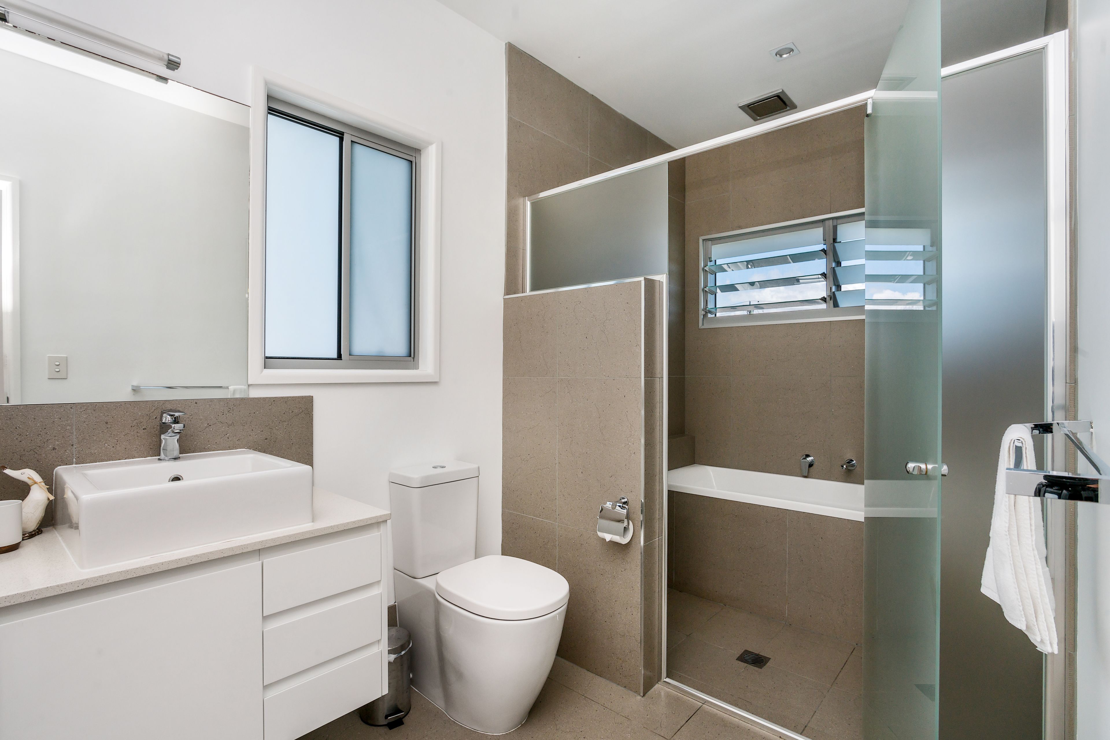 Un baño moderno con un lavamanos grande, inodoro y ducha con mampara de vidrio.