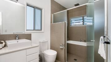 Un baño moderno con un lavamanos grande, inodoro y ducha con mampara de vidrio.