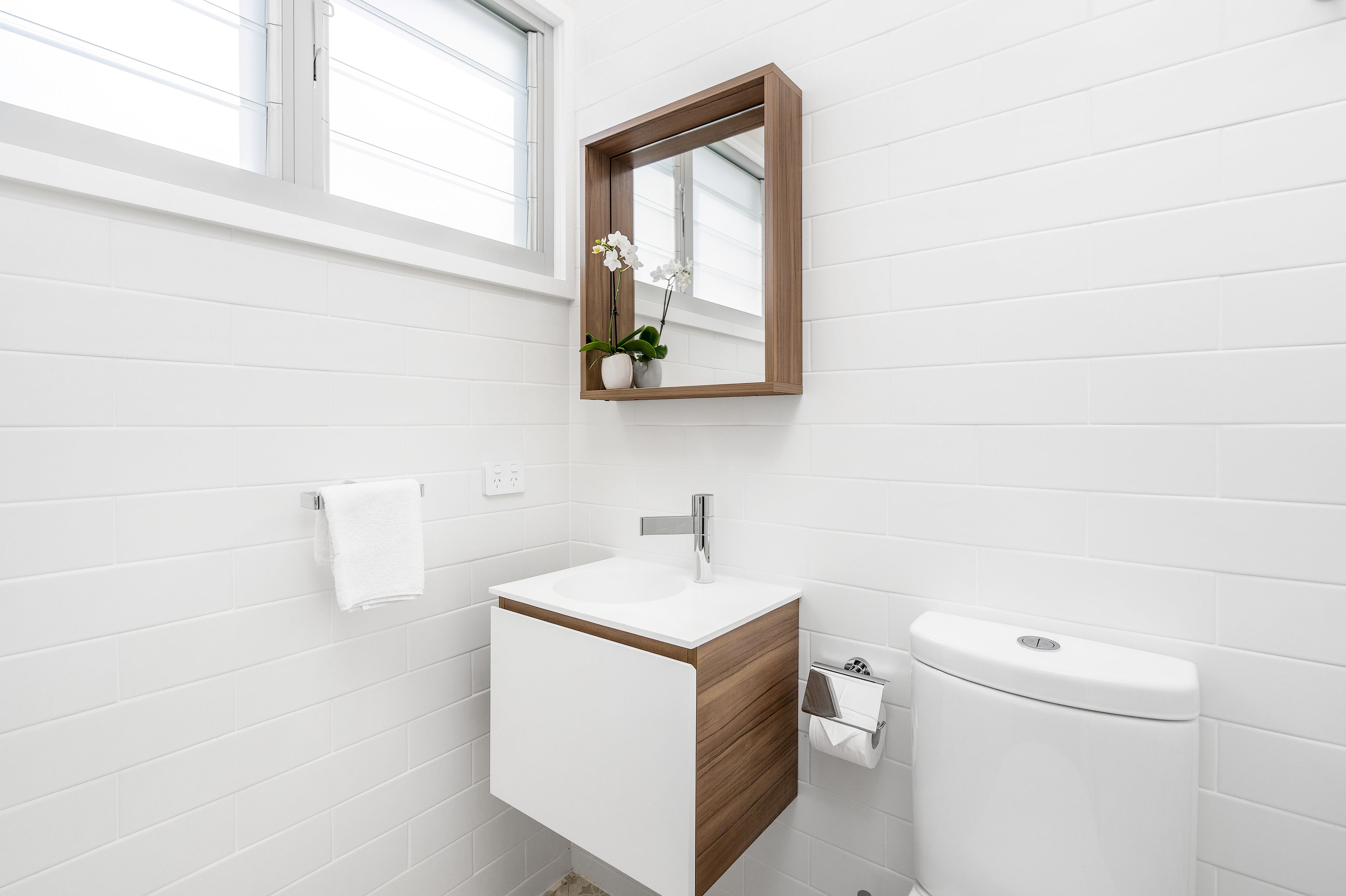 Un baño moderno con un lavamanos blanco, un mueble de madera y un espejo con marco de madera.