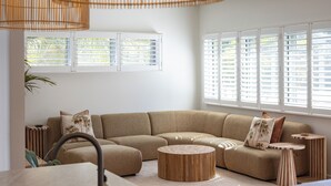 Un salon moderne avec un canapé beige, une table basse en bois et un coin cuisine équipé d’un évier.