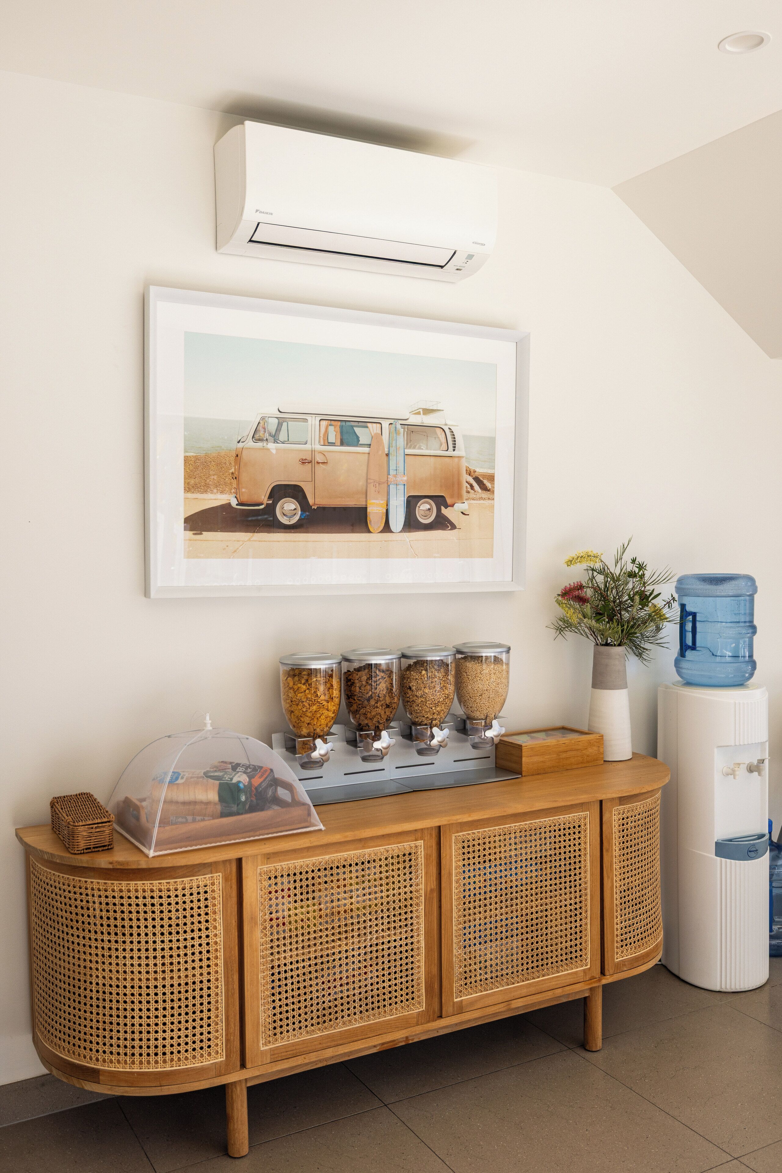 A rattan console with a clear cover, a framed vintage car picture, and a water dispenser.