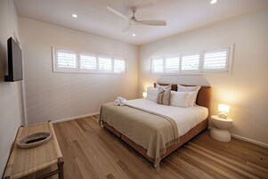Un dormitorio con cama, lámpara de noche y ventilador de techo.
