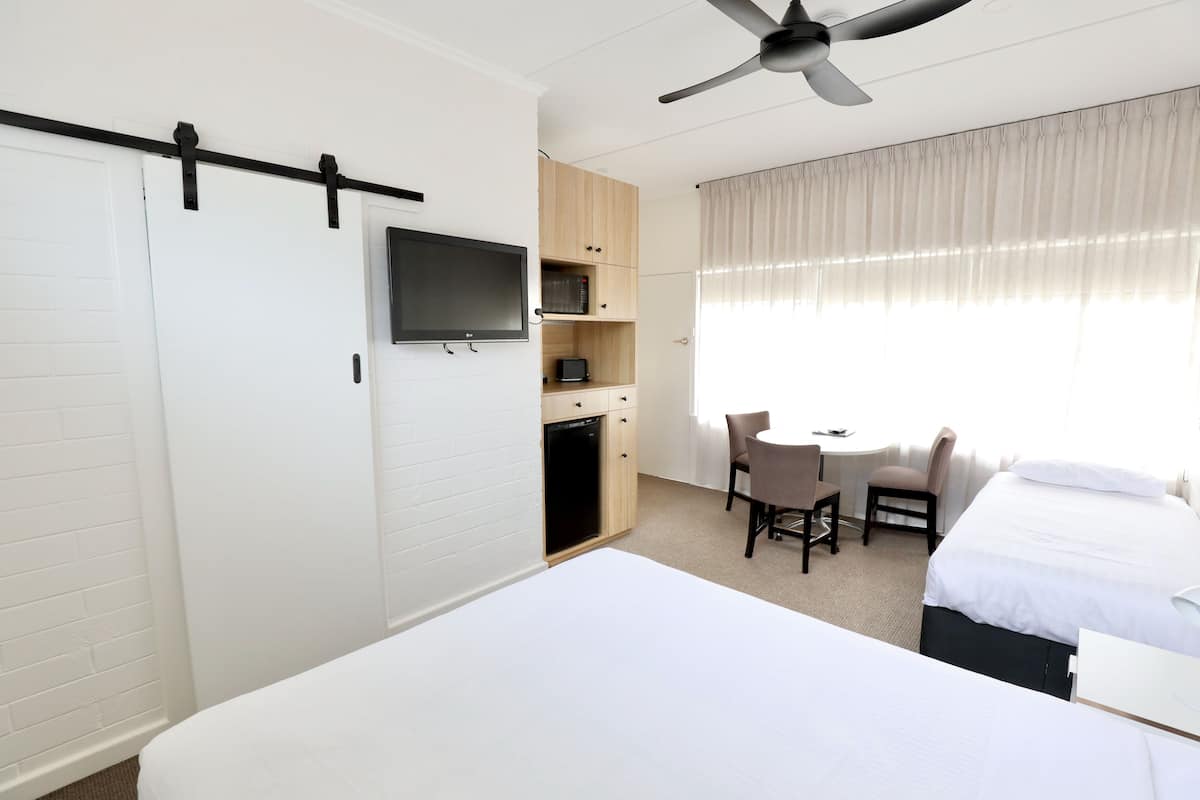 Una habitación de hotel con cama, un escritorio con silla, televisión y ventilador de techo.
