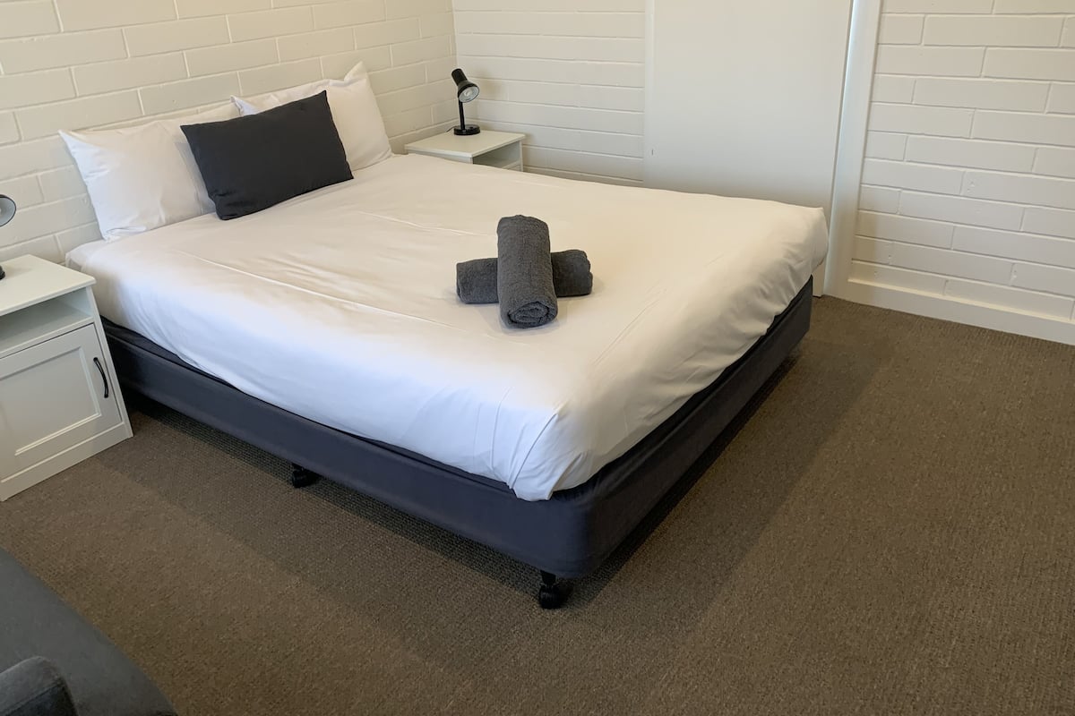 Una cama bien hecha con ropa blanca, un cabecero oscuro y una toalla gris sobre la cama.