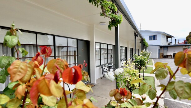 A covered outdoor area with a seating arrangement and a building with large windows. - Guichen Bay Motel (Robe)