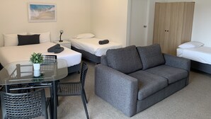 A hotel room with two beds, a grey sofa, a small table with a plant, and a chair. - Guichen Bay Motel (Robe)