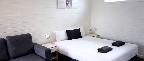 A hotel room with a bed, a chair, a nightstand, a lamp, and a window.