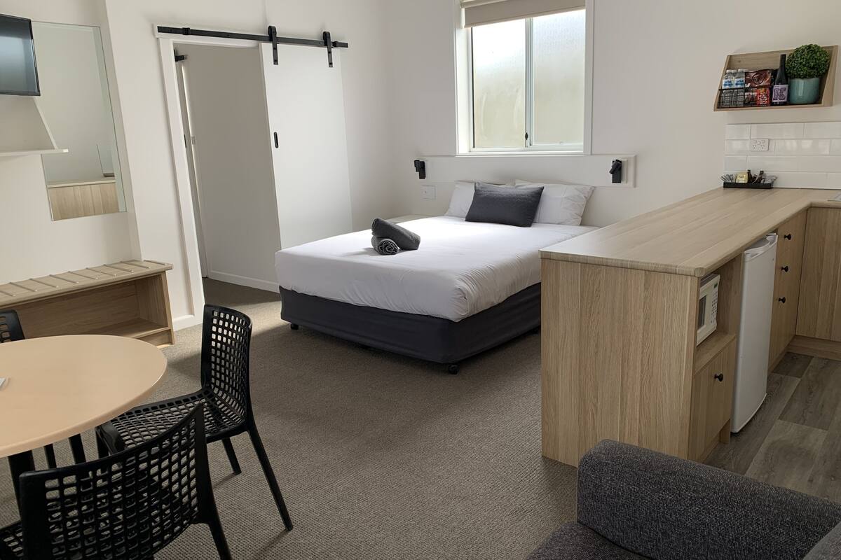 Una habitación compacta con cama, escritorio, silla, una mesita pequeña y un sofá.