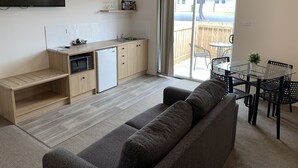 A compact kitchen with a microwave, refrigerator, and sink. There is a dining area with a glass table and chairs, and a sofa. - Guichen Bay Motel (Robe)