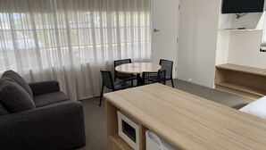 A compact hotel room with a sofa, a round table with chairs, a TV mounted on the wall, and a small wooden desk. - Guichen Bay Motel (Robe)