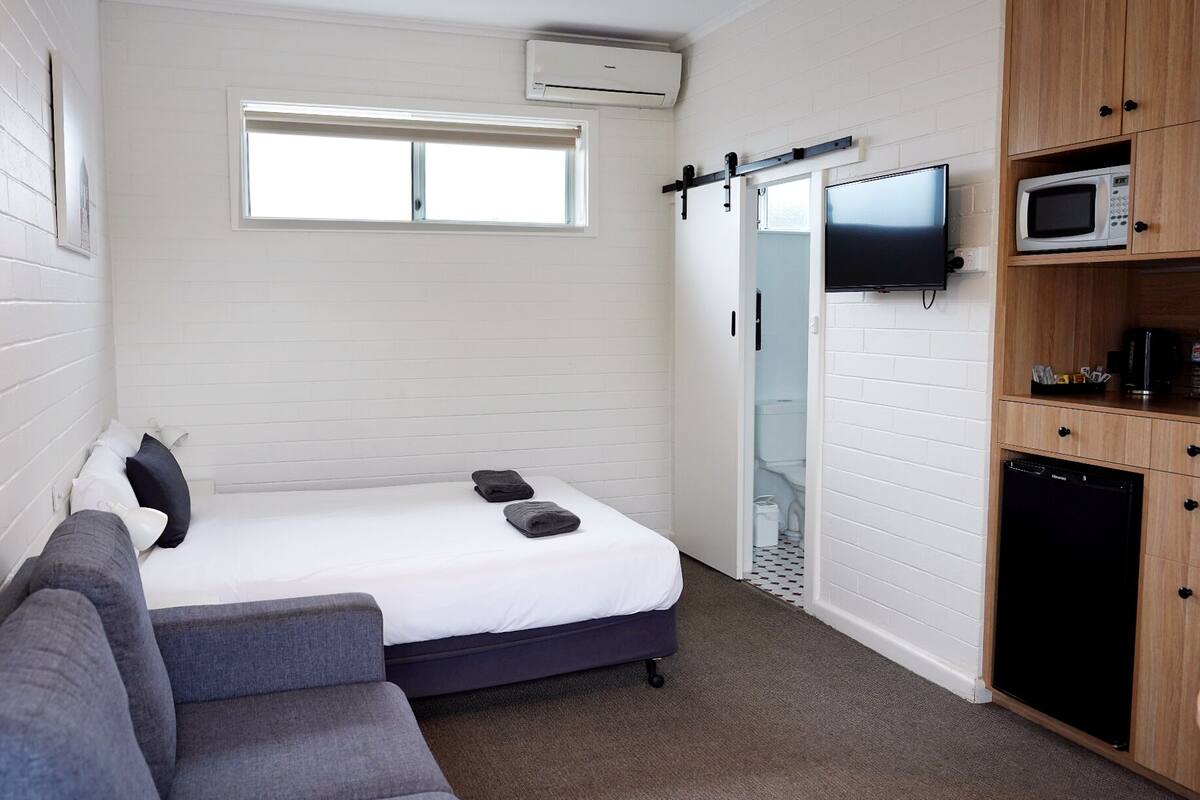 Una habitación compacta con cama, sofá, televisión, microondas y refrigerador.