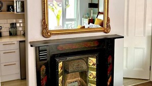 A room with a fireplace, a large ornate mirror, and a modern kitchen in the background.