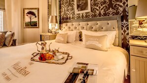 A well-appointed hotel room with a large bed, a decorative headboard, a tray with breakfast items, and a framed picture on the wall.