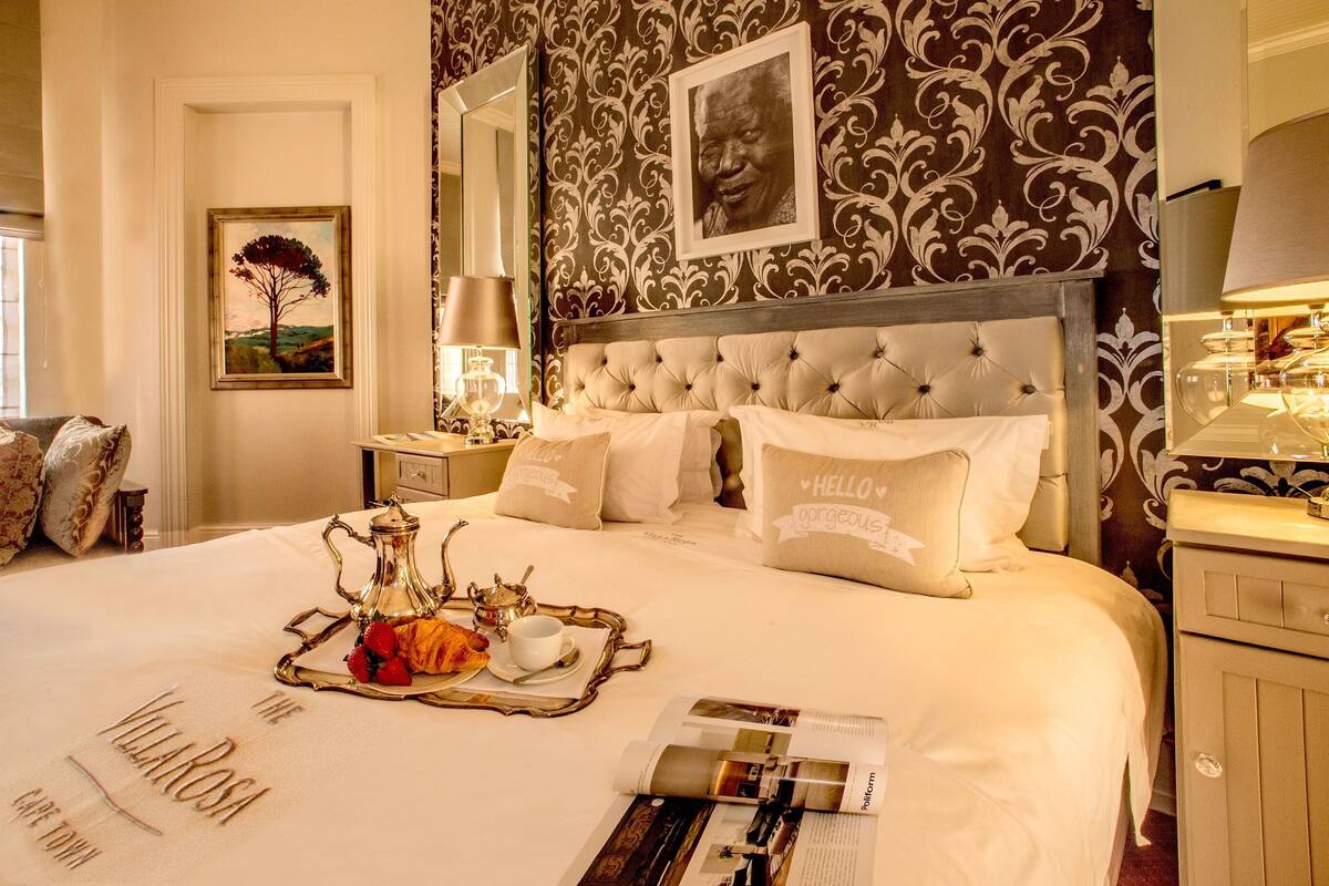 Una habitación de hotel elegante con una cama grande, un cabecero decorativo, una bandeja con productos de desayuno y un cuadro en la pared.