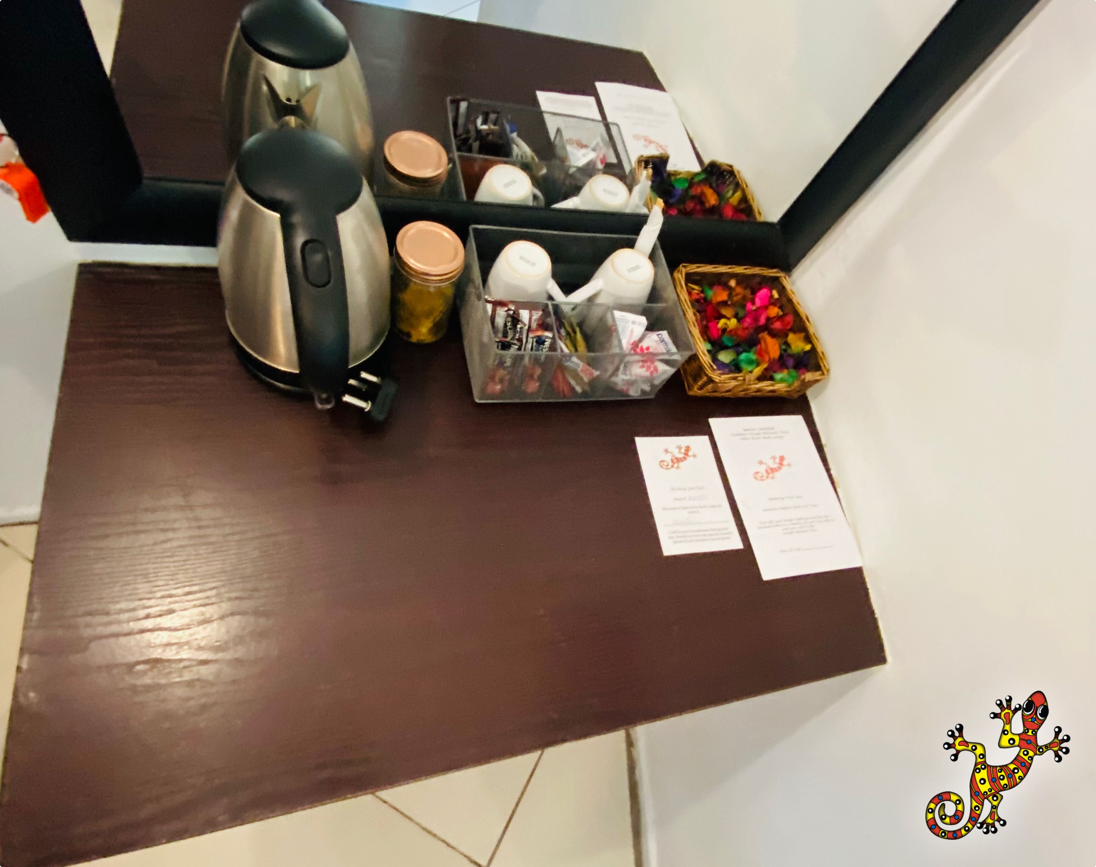 A wooden table with a coffee maker, jars, a basket of colorful items, and two printed papers.