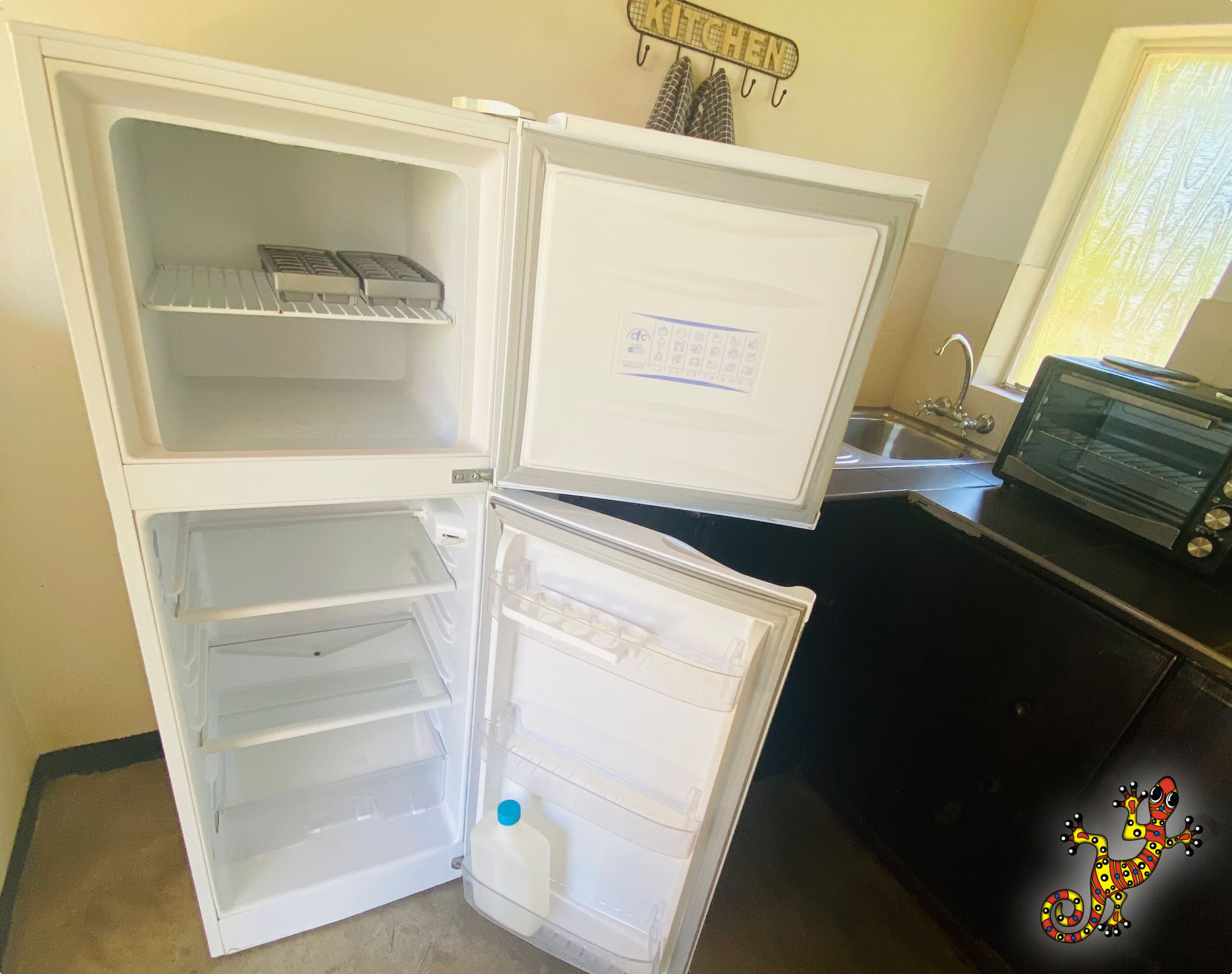 Geladeira aberta com prateleiras e um recipiente de leite no interior, pia de cozinha e um forno elétrico na bancada.