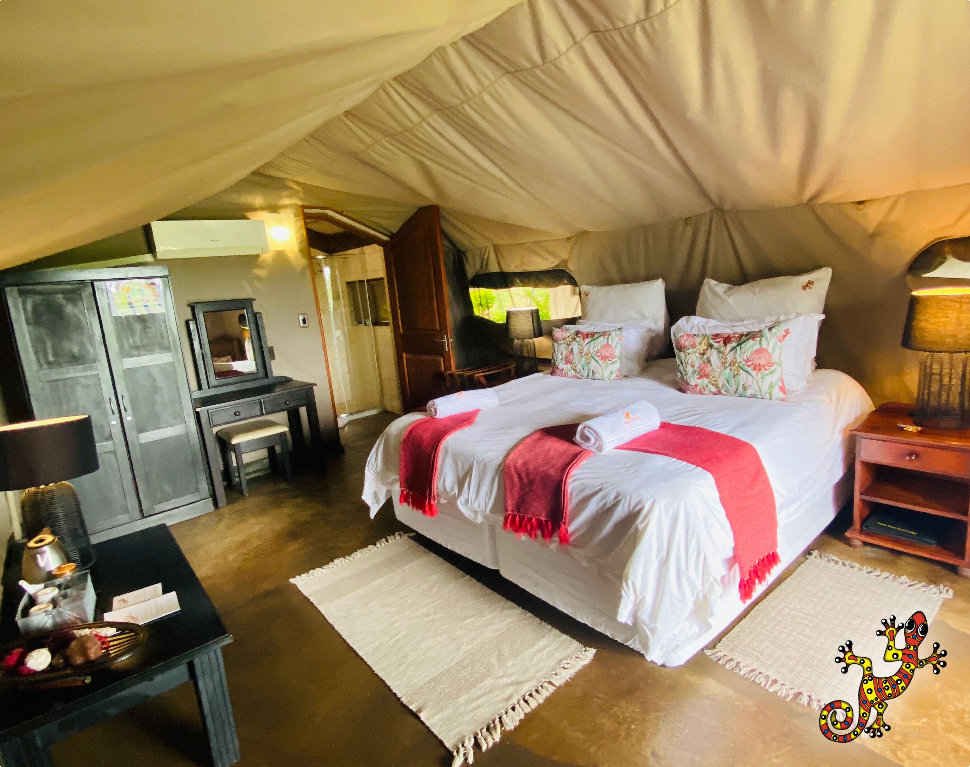 A tent-style bedroom with a bed, bedside table, lamp, and a desk with a chair.