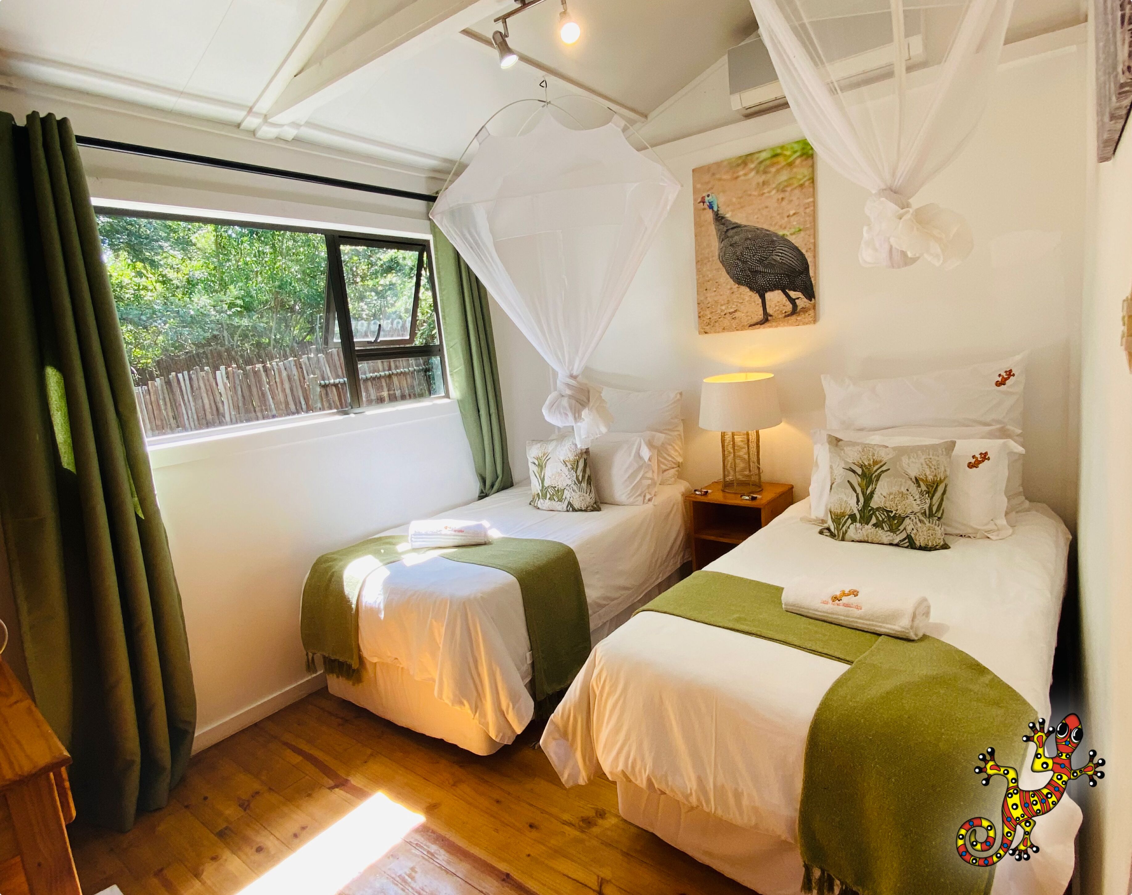 A bedroom with two single beds, a nightstand with a lamp, a window with curtains, and a wall-mounted picture of a bird.