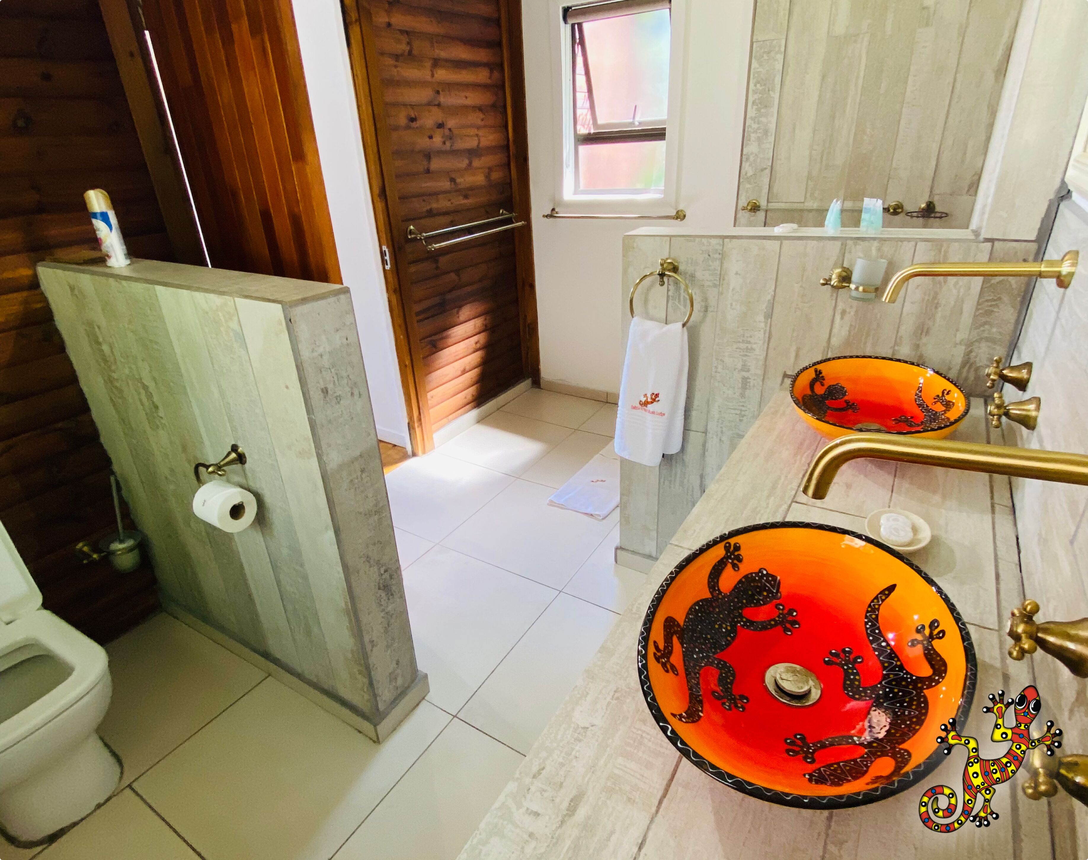 Un baño con puerta de madera, un inodoro, un lavamanos con lavabo naranja y un perchero para toallas.