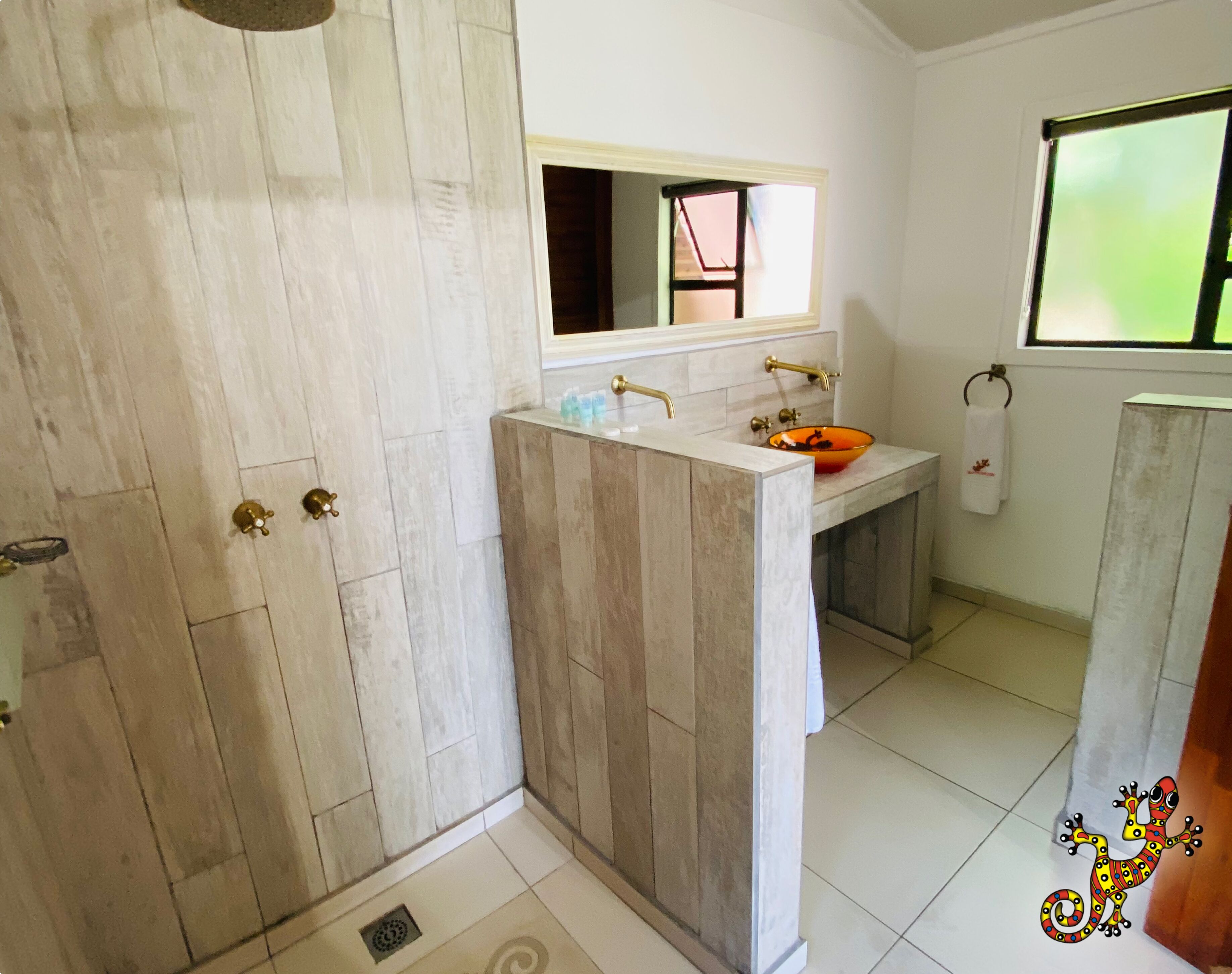 A bathroom with a wooden vanity, a sink with a glass bowl, a mirror above the sink, and a window with a view of greenery.
