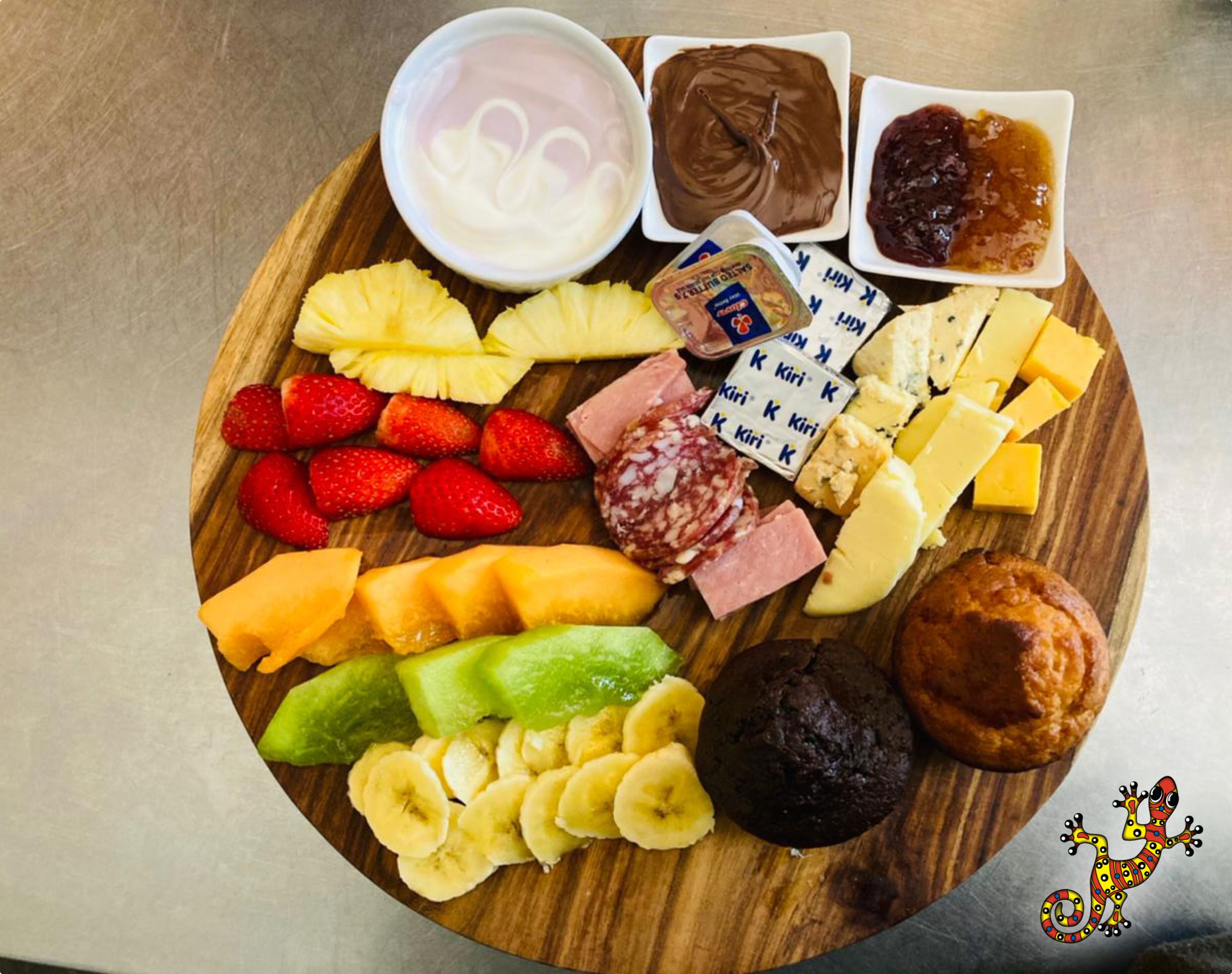 Ein Holzbrett mit verschiedenen Speisen, darunter Obst, Käse und ein Muffin.