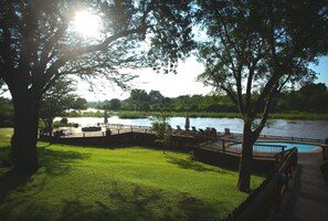 A riverside park with a wooden deck, a swimming pool, and lush greenery.