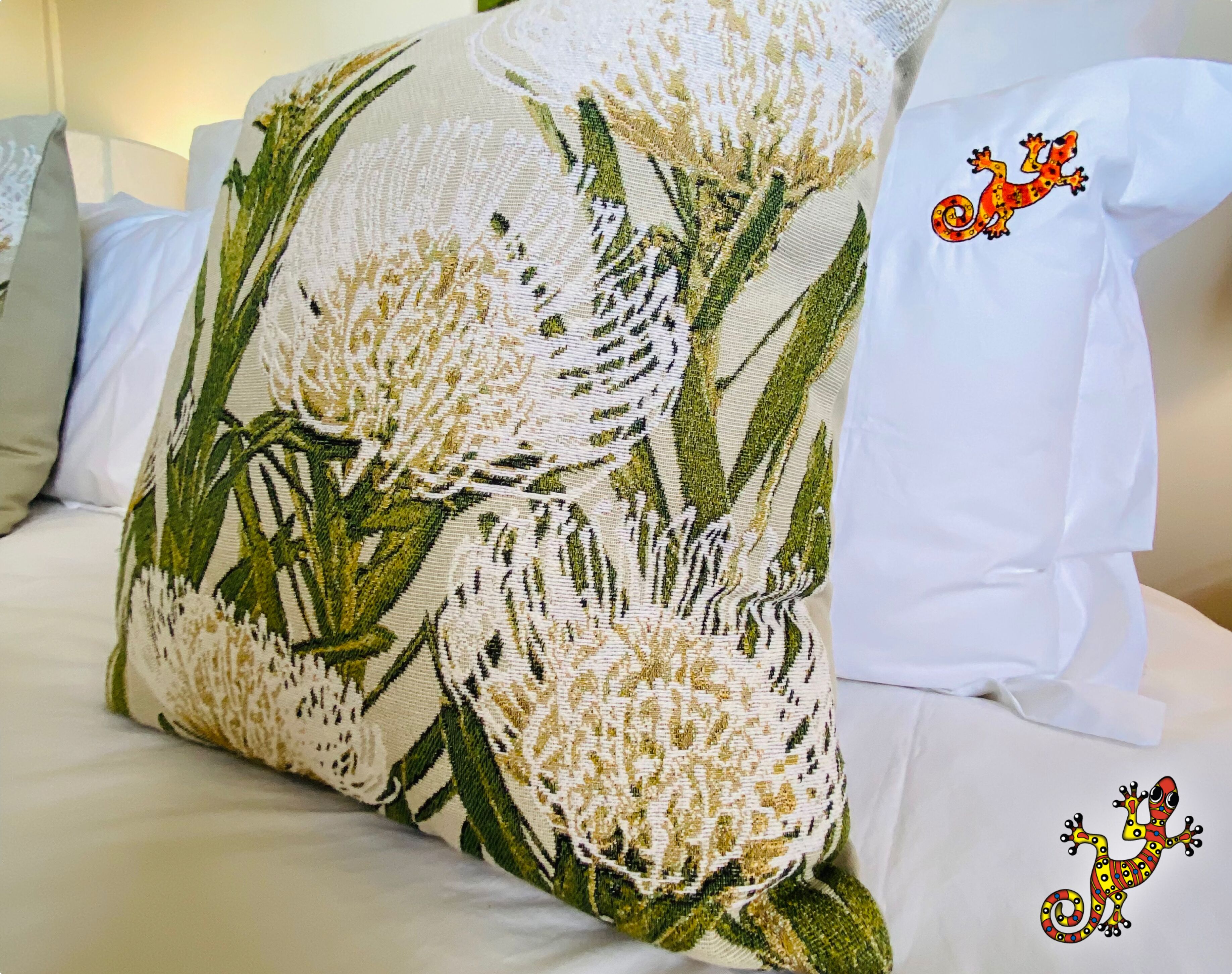 Un almohadón con estampado floral sobre una cama con ropa de cama blanca.