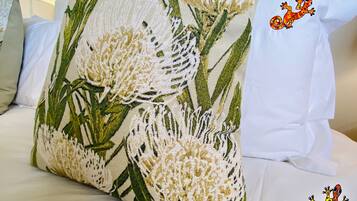 Un almohadón con estampado floral sobre una cama con ropa de cama blanca.
