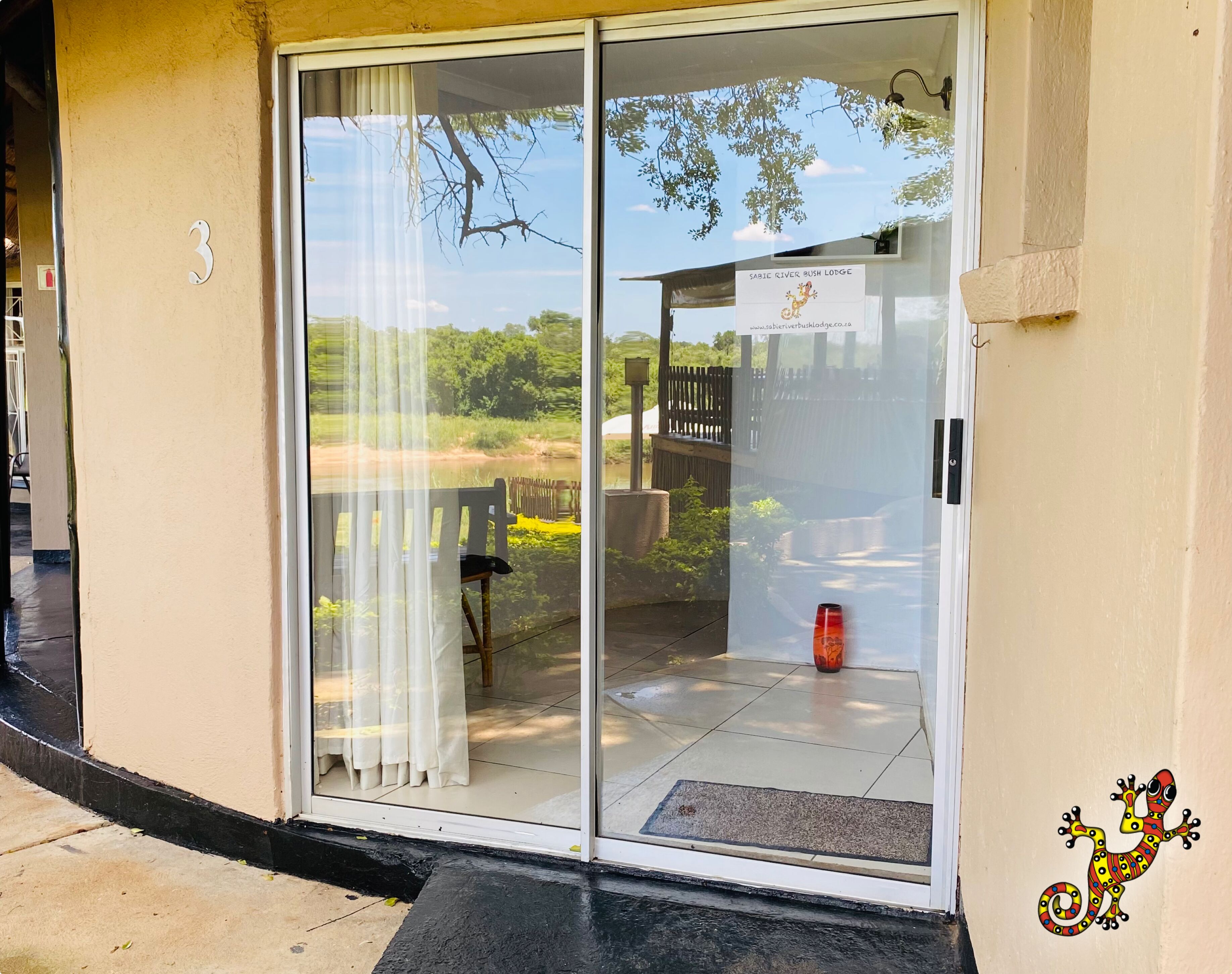 A sliding glass door leading to a patio with a chair and a red vase.