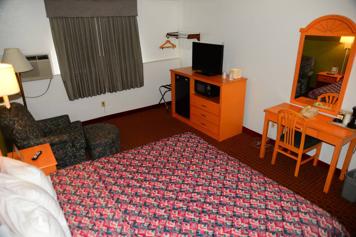 Habitación de hotel con cama, escritorio, silla, cómoda, televisor y espejo.
