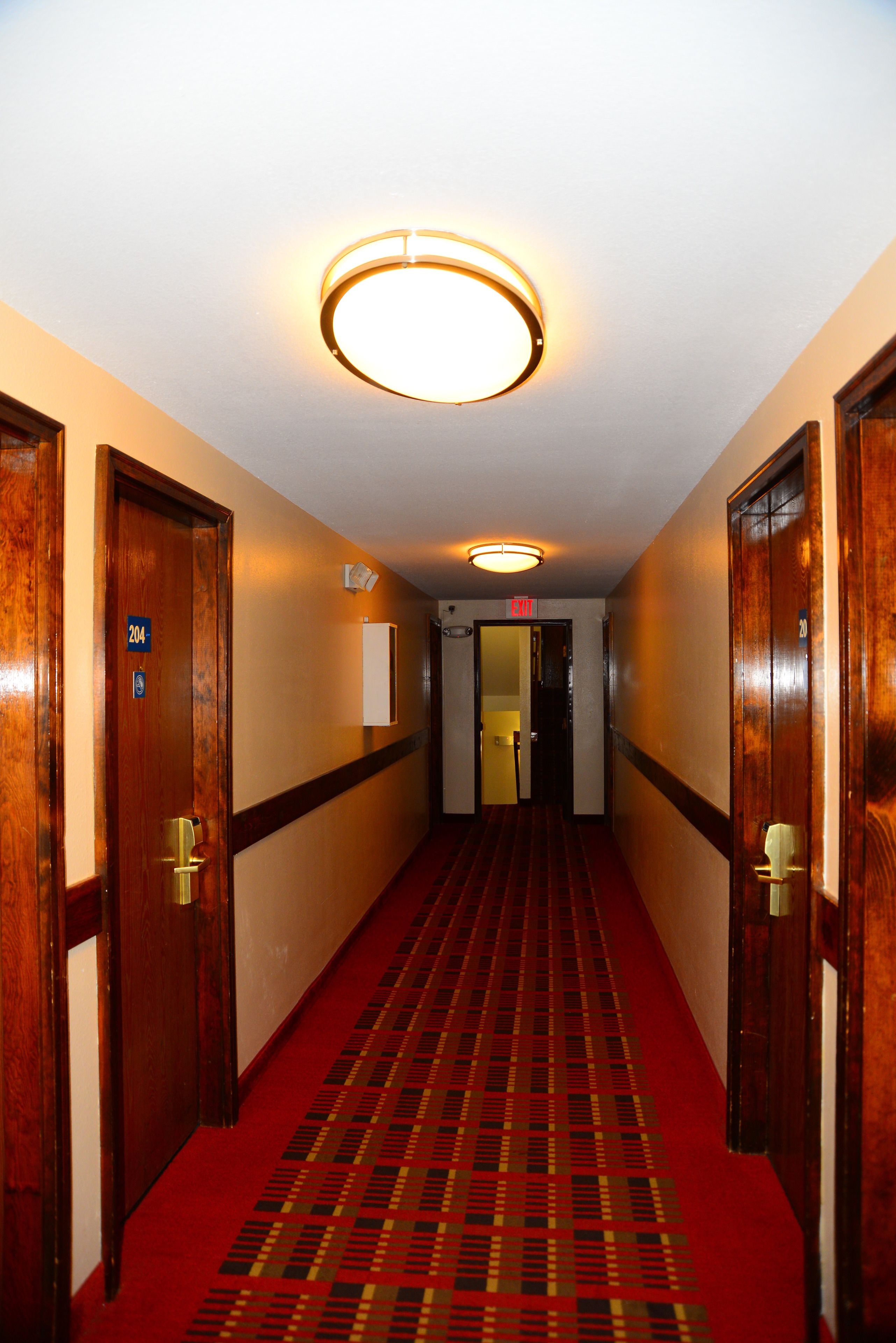 A hotel hallway with wooden doors, a red carpet, and a ceiling light fixture.