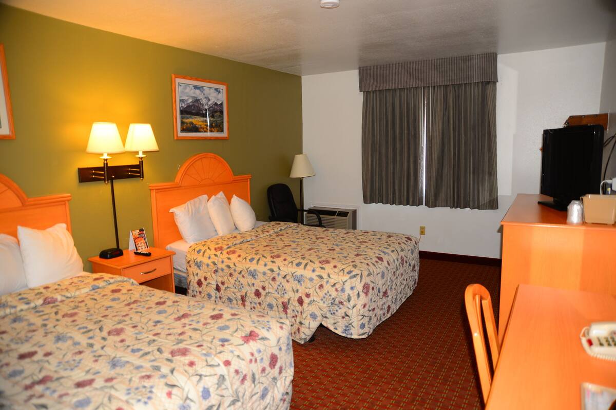 Habitación de hotel con dos camas, un escritorio, una silla, un televisor y una ventana con cortinas.
