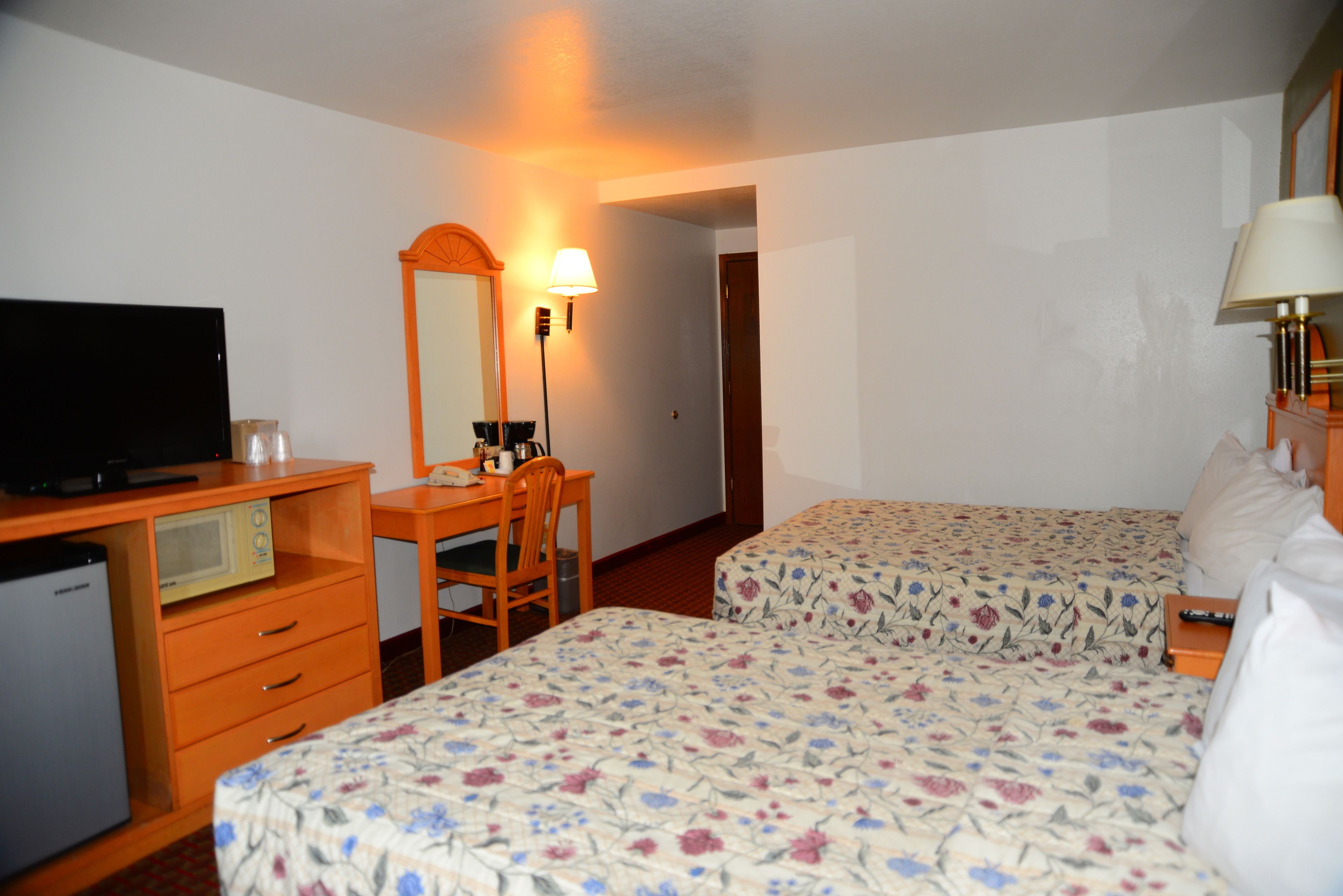 A hotel room with two beds, a desk with a chair, a television, and a mirror.