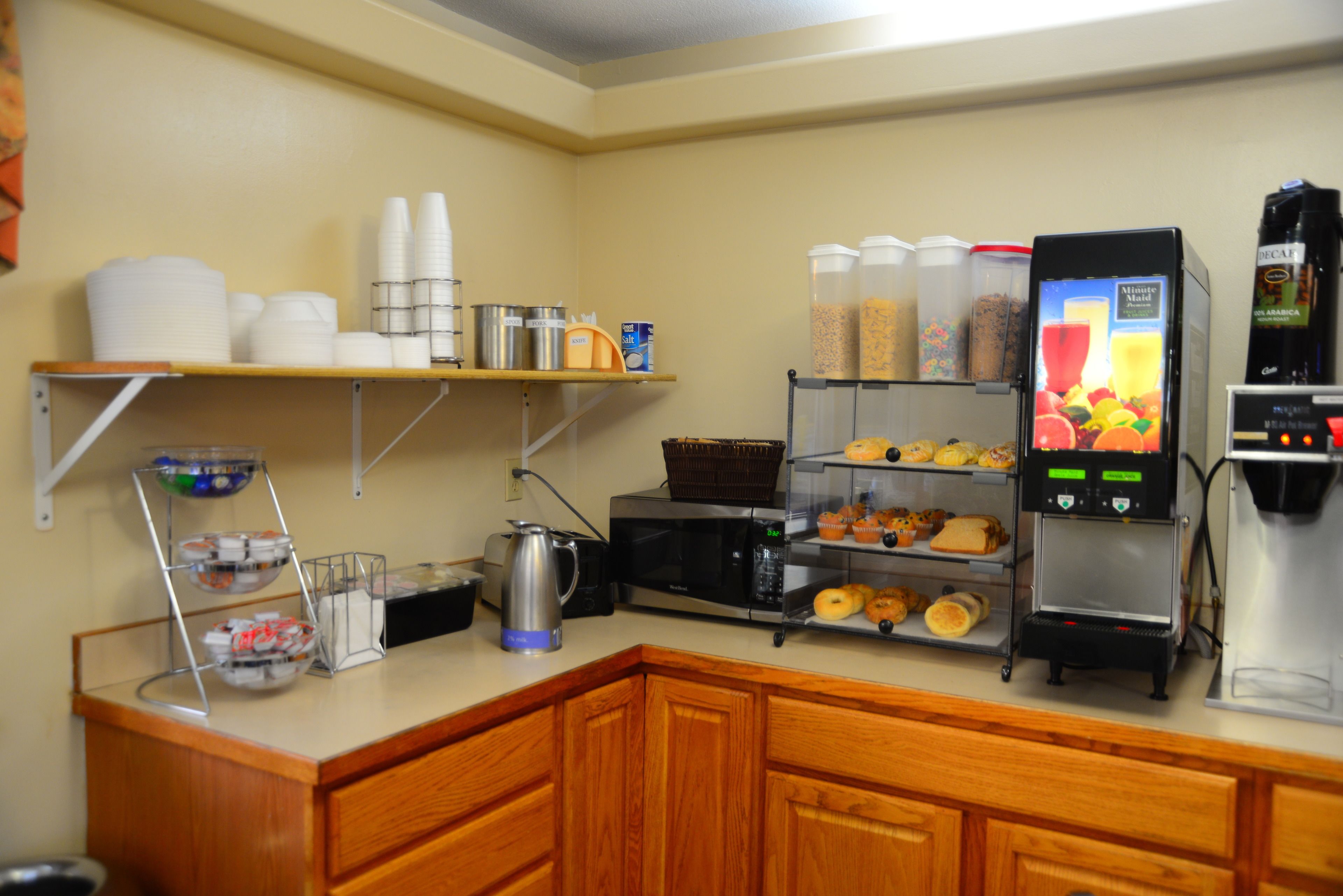 Een kitchenette met een koffieapparaat, een magnetron en planken met etenswaren.